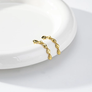Detail of gold asymmetric tassel earrings with pebble-shaped drops on white ceramic