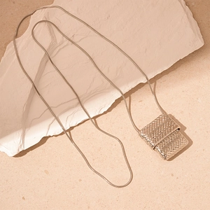Close-up of silver woven bag pendant on snake chain over textured stone background