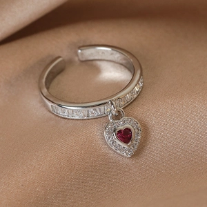 Macro shot of a silver open ring with red heart pendant on champagne silk background