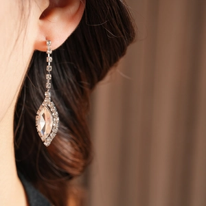 Close-up of a silver drop earring with sparkling rhinestones and a large oval gem on a model