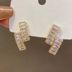 Macro shot of geometric gold earrings with baguette-cut crystals and a layered design