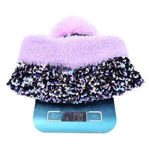 Bonnet à paillettes avec pompon en fourrure sur une balance affichant un poids de 130g