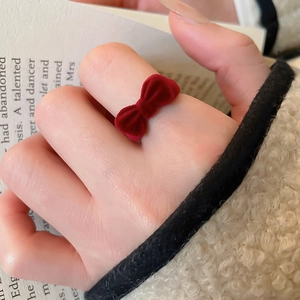 Detail view of a vintage red flocked velvet bow ring on a finger with a cozy winter vibe