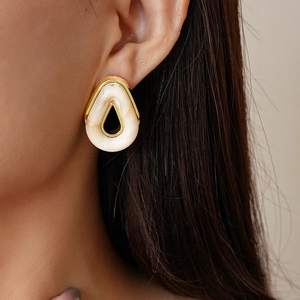 Close-up of a hollow teardrop earring with cream resin and gold trim worn by a model