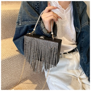 Detail view of black rhinestone clutch bag with long tassels held by a model on stairs