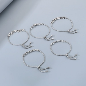 Flat lay of five adjustable silver stainless steel bracelets with various trendy charms