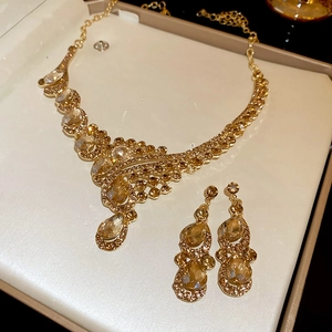 Close-up of golden necklace and earrings set with amber teardrop crystal pendants