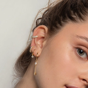 Close-up of gold-plated earrings set with cubic zirconia layered on model's ear