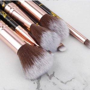 Detail of soft synthetic bristles and rose gold ferrules on marble makeup brushes
