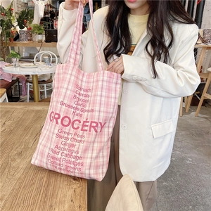 Pink checkered canvas tote bag with GROCERY text carried by a model in a cozy setting