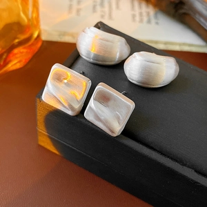 Macro shot of silver brushed metal square and C-shaped earrings on textured black box