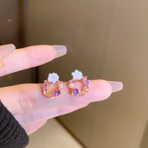 Detailed close-up of rose gold floral earrings with purple crystals and white pearls