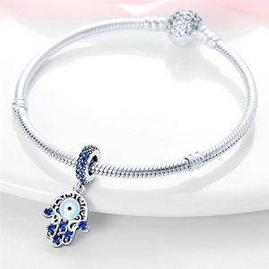 Macro shot of silver Hamsa Hand charm with blue and white stones on a porcelain tray