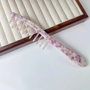 Close-up of wide-tooth acetate massage comb with purple and white marbled texture on tray