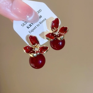 Detail of red flower earrings with white zircon core and red pearl droplet on gold metal