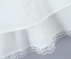 Detailed close-up of the delicate white lace trim on the white cotton linen dress hemline
