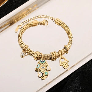 Golden Hamsa Hand bracelet with blue evil eye pendant on a reflective surface