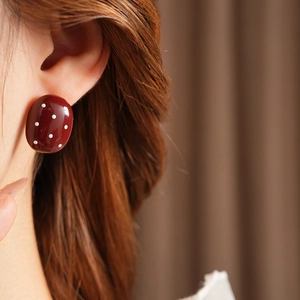 Primo piano di orecchini ovali marrone rosso con pois bianchi indossati da una modella