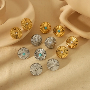 Modern gold and silver steel stud earrings with sunburst texture and pearls on linen