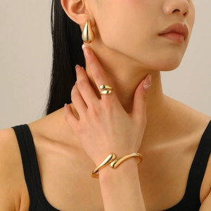 Detail view of mirror finish gold teardrop jewelry set featuring earrings, ring and bangle