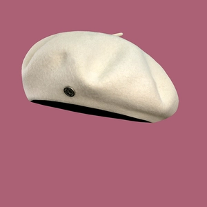 Detailed view of off-white wool beret with a round metallic side buckle on a soft background