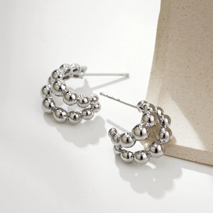 Polished silver double-row bead C-shaped hoop earrings on a textured stone display