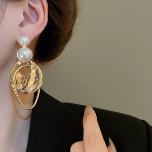Close-up of model wearing chunky irregular gold hoops with double pearls on ears