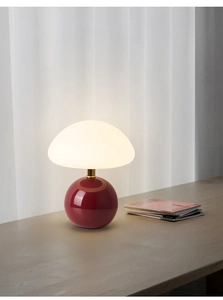 Detail of mushroom lamp with creamy white shade and glossy red base on a wooden desk