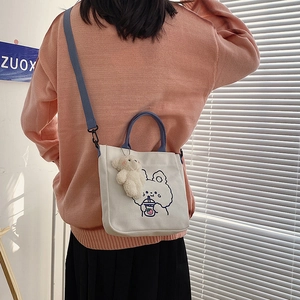 Detail of white canvas tote bag with blue cartoon bear print and plush toy accessory