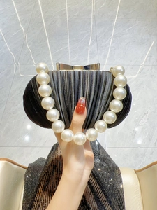 Detail der schwarzen Abendtasche mit Perlengriff und goldener Schleife im Muschel-Look