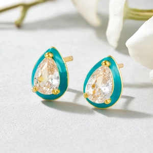 Macro detail of teardrop earring featuring gold base with cyan enamel and white stone