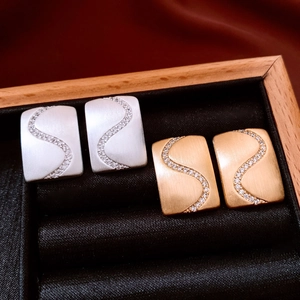 Detail of matte rectangular stud earrings with S-shaped zircon inlay in gold and silver