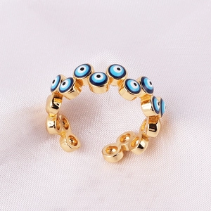 Macro shot of gold-plated evil eye rings with blue enamel inlay on white silk fabric