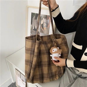 Detailed view of brown plaid wool tote bag with a cute bear charm on a display shelf