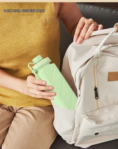Collapsible silicone water bottle in light green being placed into a beige backpack pouch