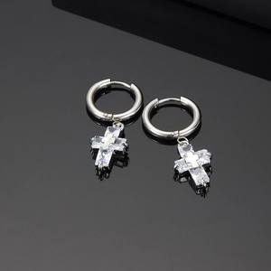 Macro shot of silver cross pendant earrings with zircon stones on a black reflective base