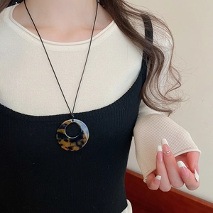 Close-up of tortoiseshell resin ring pendant necklace on model with black cord strap