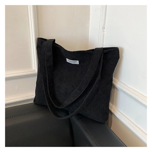 Detail of minimalist black corduroy tote bag with white Fashion label on leather sofa