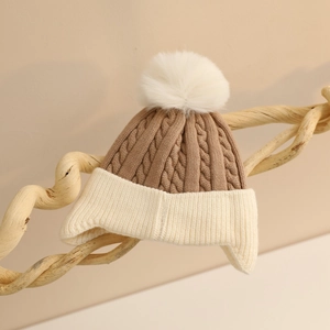 Detail of baby winter knit hat with cable pattern, color-block earflaps and fur pompom