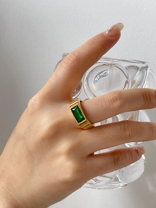 Macro detail of gold-plated striped ring featuring a rectangular emerald green gemstone