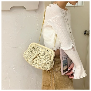 Model wearing a hand-woven straw clutch bag with a gold metal chain strap on a white wall