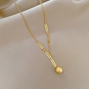 Detail of gold titanium steel necklace with a frosted ball pendant on soft beige fabric