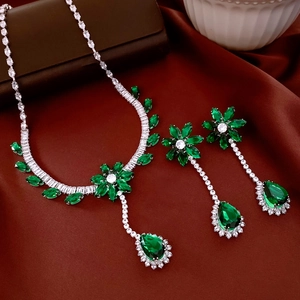 Détail du collier et des boucles d'oreilles fleur émeraude sur fond de soie rouge