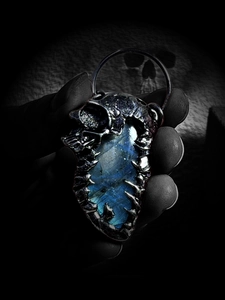 Macro shot of a gothic skull pendant with glowing blue labradorite in vintage silver finish