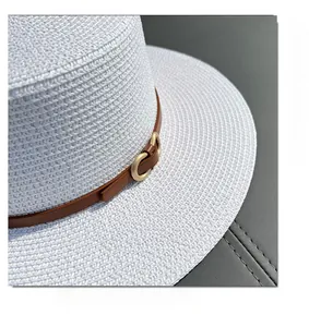 Detail of white straw hat with fine weave and brown leather strap featuring gold buckle