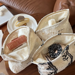 Detail of beige lace embroidery cosmetic bags with zippers on a wooden table