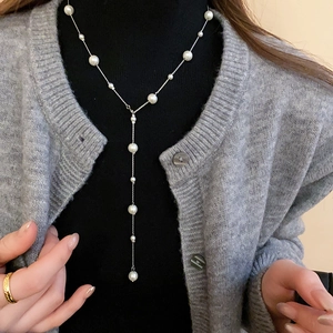 Detailed view of elegant white pearl Y-necklace styled on a grey sweater
