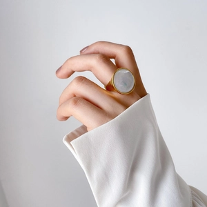 Detail of a large round white shell stone set on a thick gold minimalist ring on a hand