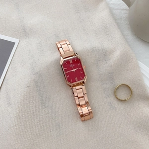 Detail of rose gold rectangular watch with red dial and Roman numerals on fabric