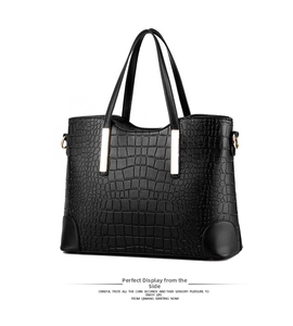 Detail of black faux leather tote bag with crocodile pattern and golden metal bar